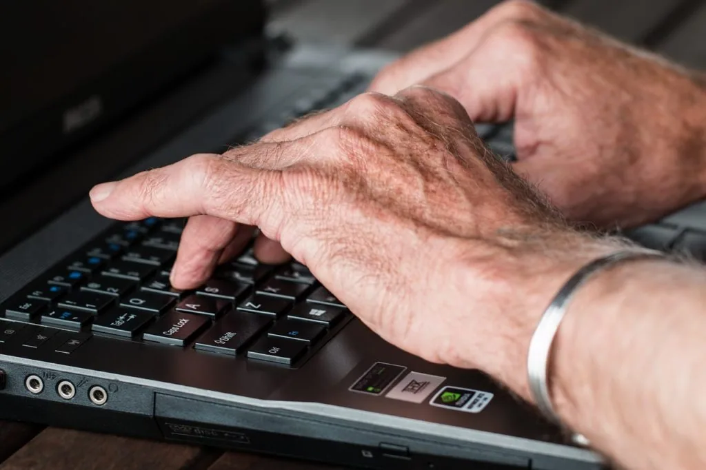 Mature person typing on a laptop keyboard with one hand visible
