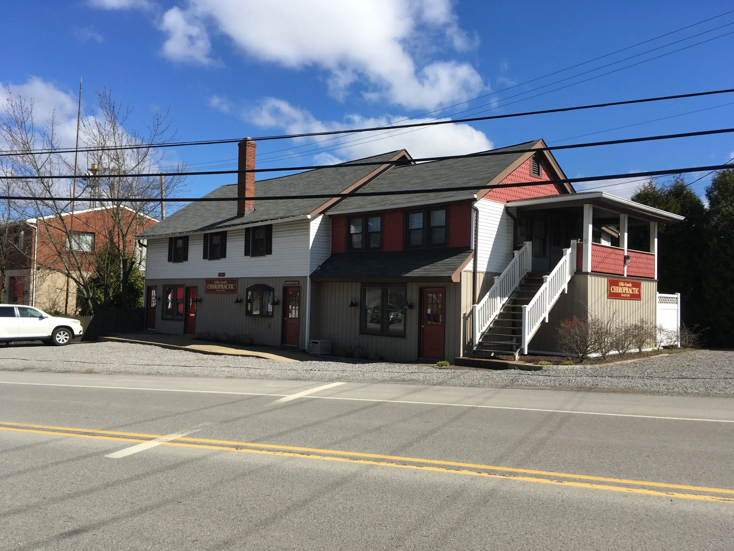 Multi-story commercial building with white and red siding, red doors, and covered entrance stairs on a street corner with power lines overhead.